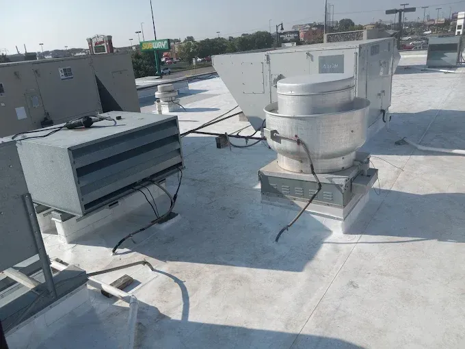 Rooftop with HVAC units. Gray metal boxes and vent on white roofing. Sunny day.