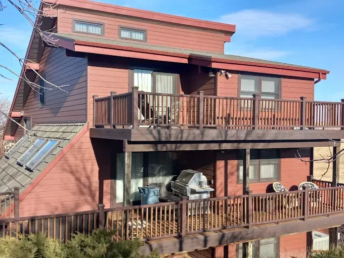 Two-story red house with multiple decks, overlooking the landscape, clear sky.