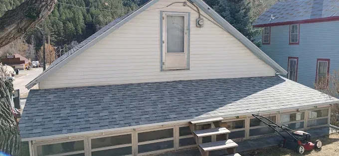 A two-story house with a sloped roof and an enclosed porch; a lawnmower sits outside.
