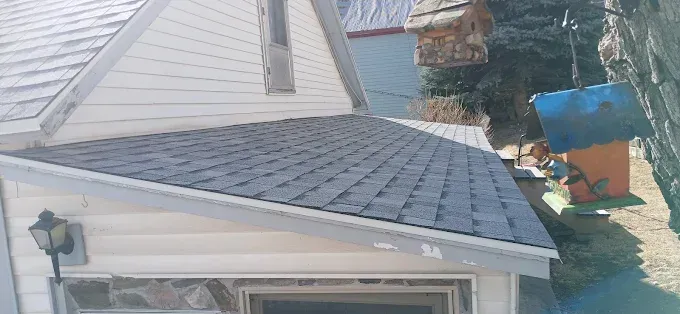 A house with a gray roof and white siding, a bird feeder, and trees in the background.
