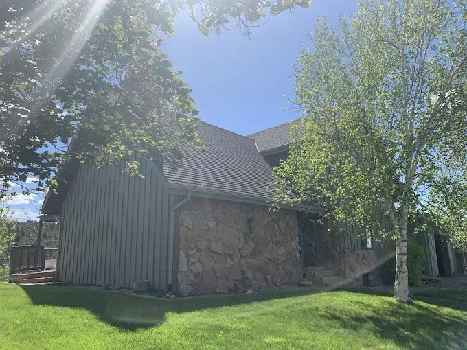 House with stone and wood siding, green lawn, and trees under a bright blue sky.