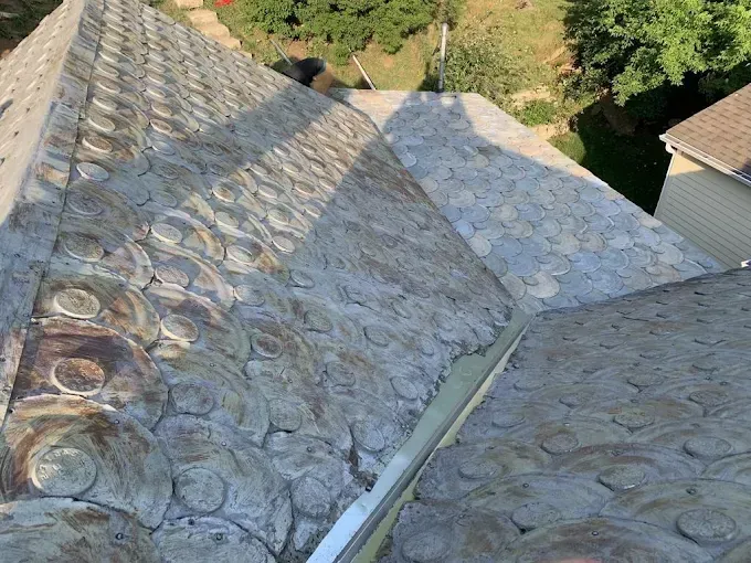 Overhead view of a textured, gray, circular-patterned roof with metal flashing. Sunlight casts shadows.