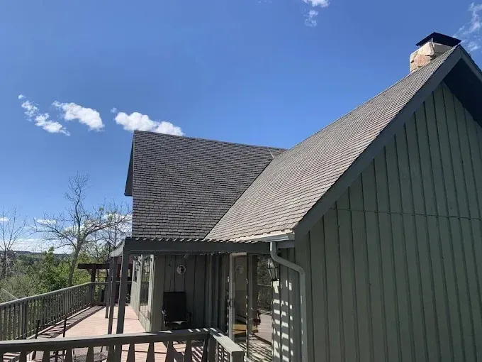 Green house with a dark shingle roof, wooden deck, and blue sky.