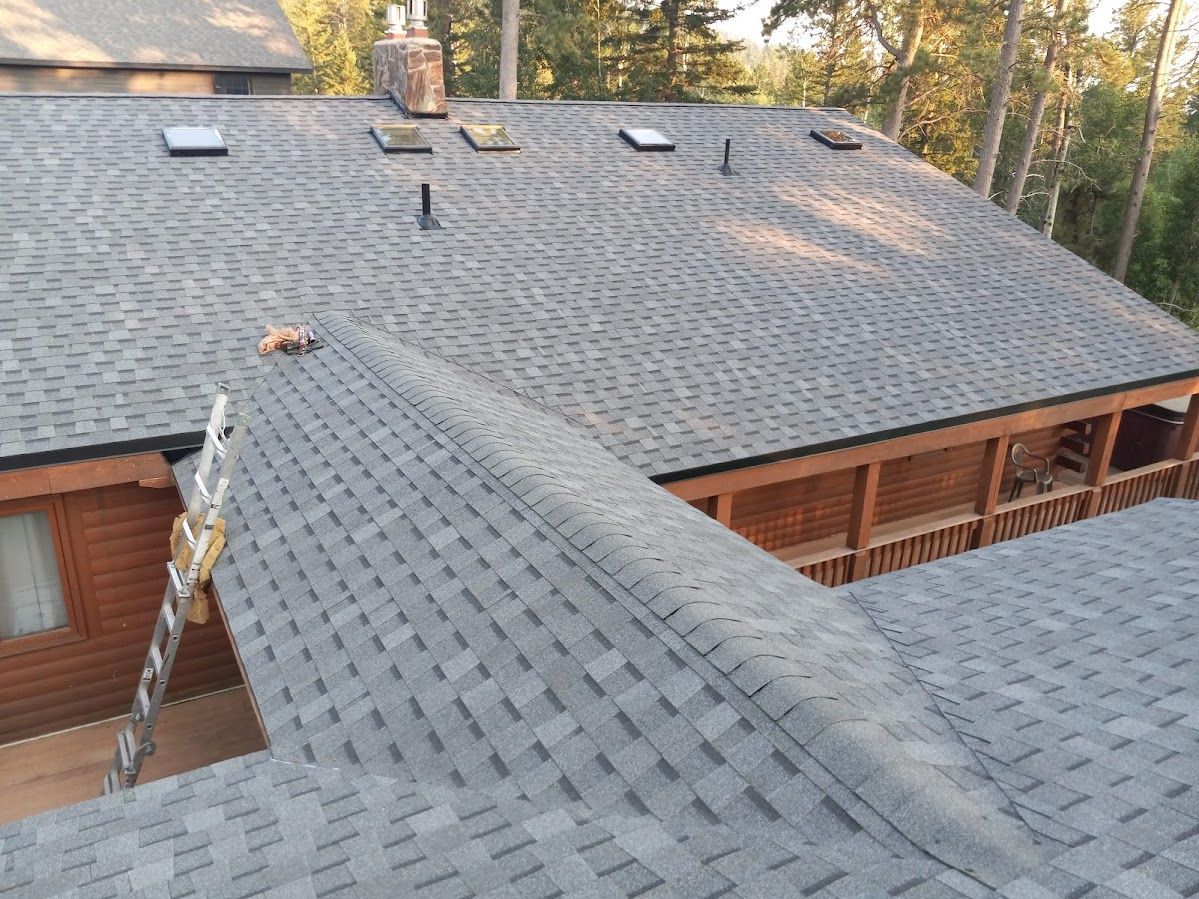 Gray shingle roof on a house with skylights and a wooden porch; trees in the background.