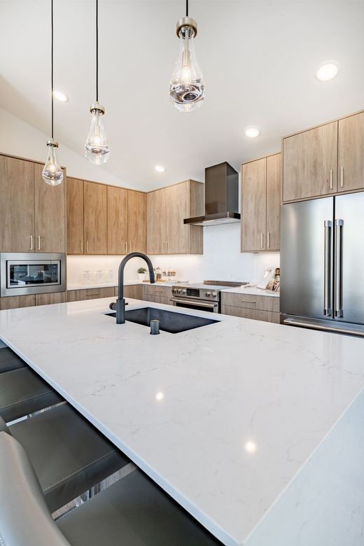 Modern kitchen with a large white island, wooden cabinets, and stainless steel appliances.