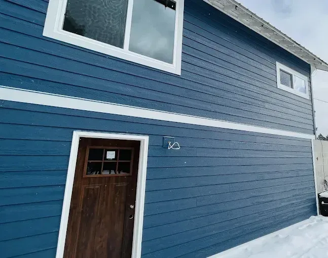 Blue house with white trim, wooden door, and snow on the ground.