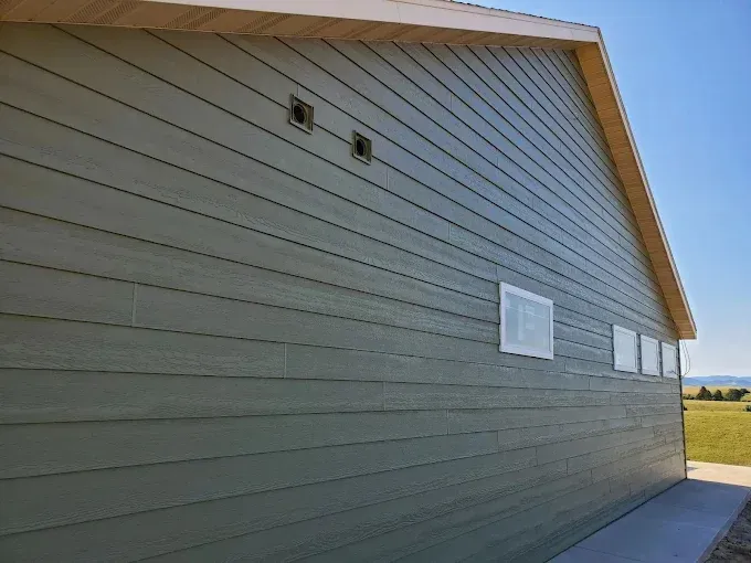 Green-sided building with horizontal wood-like siding, vents, and windows, under a blue sky.