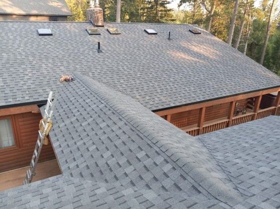 Gray shingle roof on a blue house with a chimney, overcast sky.