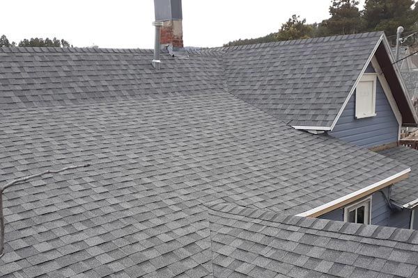 Gray shingle roof on a blue house with a chimney, overcast sky.