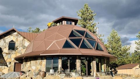 Stone and dome home with triangular windows, brown roof, sunny day, mountains in background.