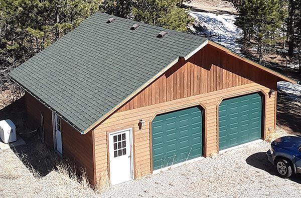 Two-car garage with green doors and a green roof; brown wood siding; white door; car parked nearby.