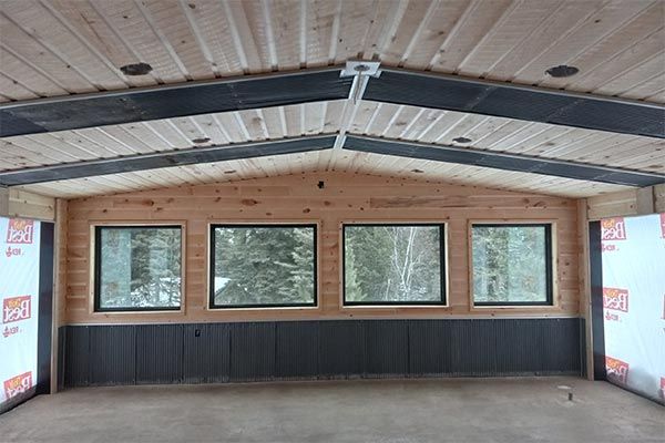 Interior of a cabin under construction, showing windows and wooden walls and ceiling.