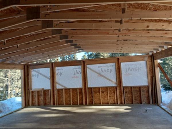 Construction of a wooden structure with concrete floor. Walls have framed windows, snowy background.