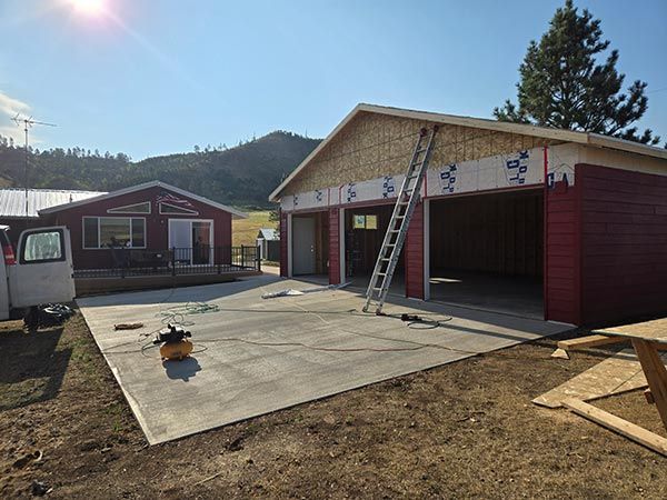 Garage under construction with red siding, unfinished roof, and concrete slab in a rural setting.