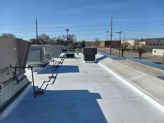 A flat commercial rooftop with HVAC units, a ladder, and a white surface under a clear, blue sky.