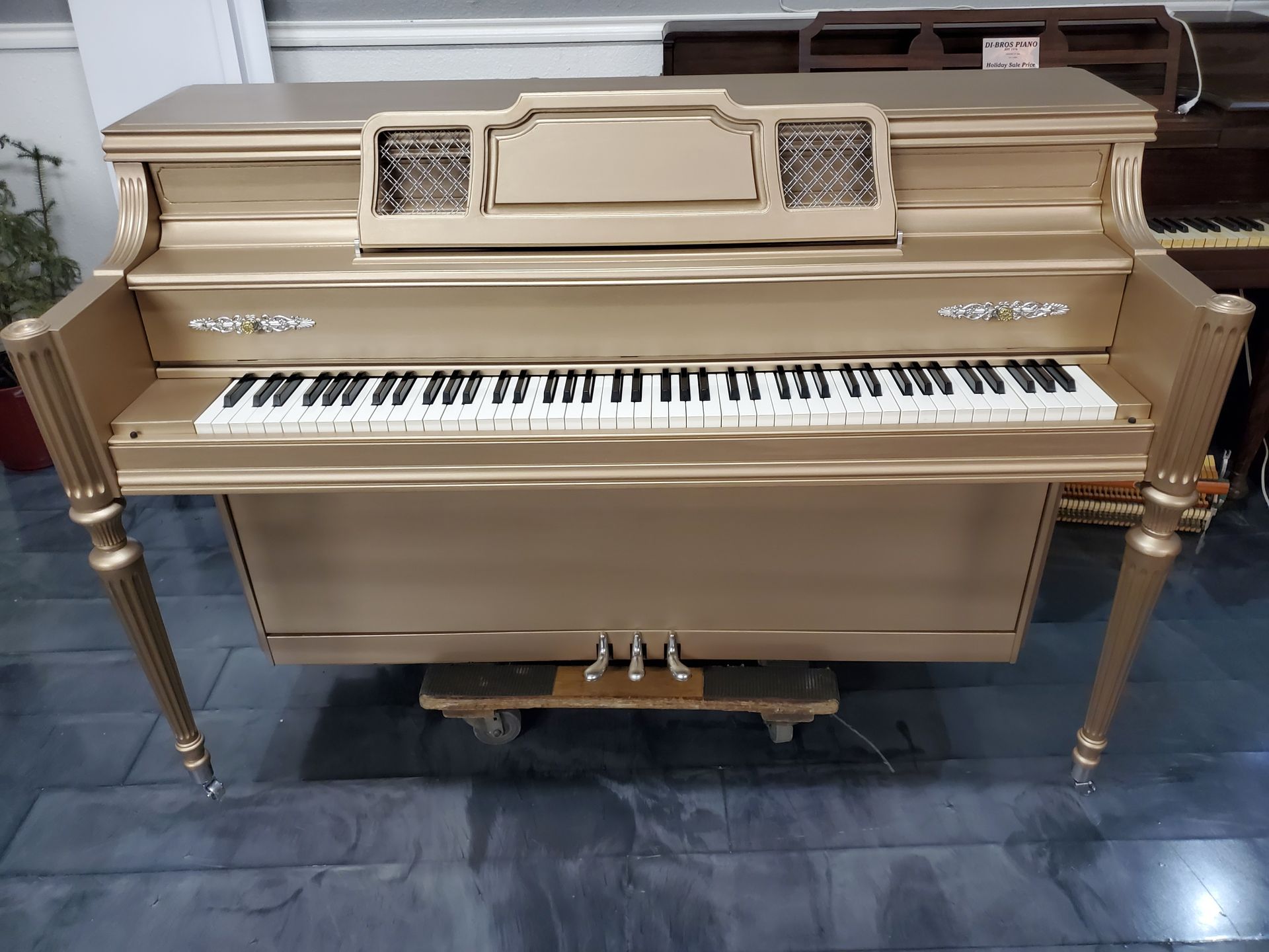 A gold piano is sitting on a tiled floor in a room.