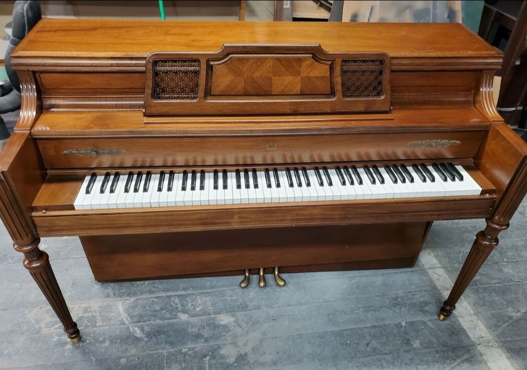 A wooden piano with white keys is sitting on a concrete floor