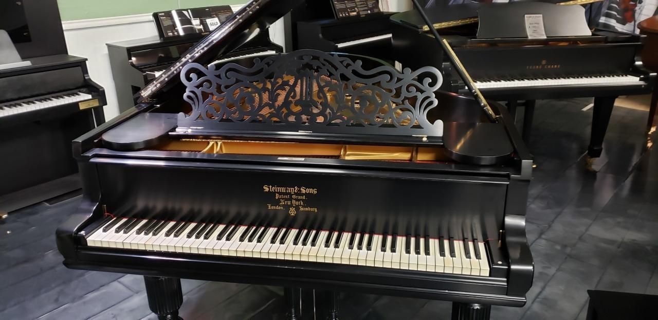 A black grand piano is sitting in a room with other pianos.