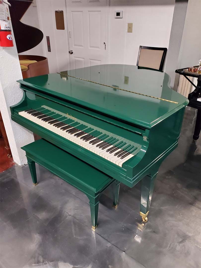 A green grand piano is sitting on a concrete floor in a room.