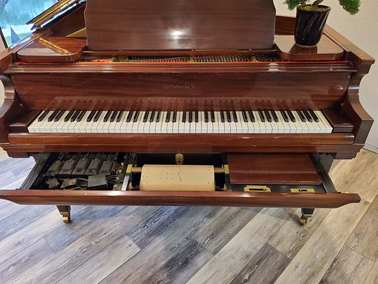 A piano with a drawer underneath it is sitting on a wooden floor.