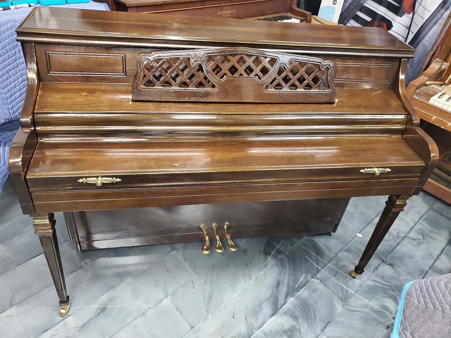 A wooden piano is sitting on a tiled floor in a room.