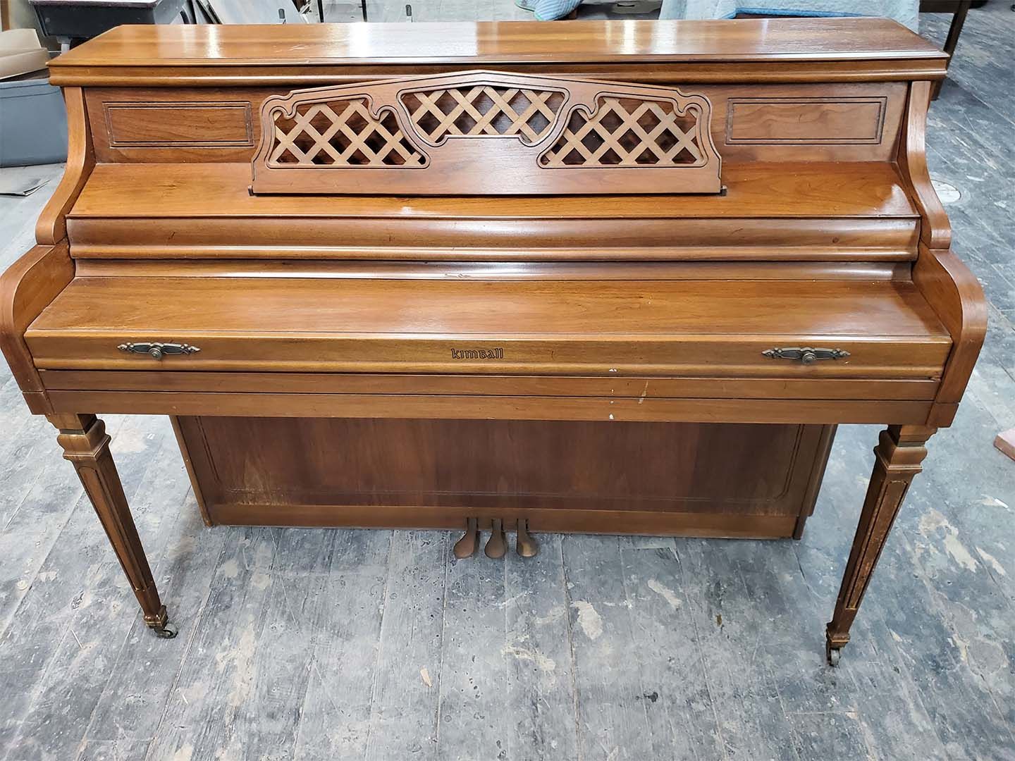 A wooden piano is sitting on a concrete floor.