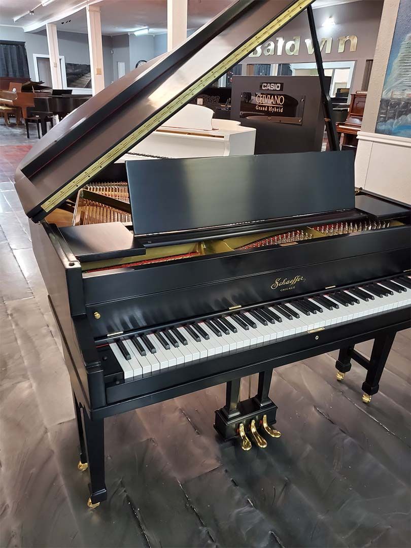 A black grand piano is sitting on a wooden floor in a store.