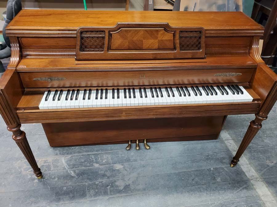 A wooden piano is sitting on a concrete floor.