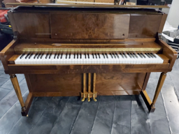 A brown piano with white keys is sitting on a tiled floor