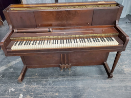 A brown piano with white keys is sitting on a wooden floor