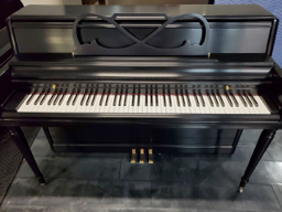 A black piano with white keys is sitting on a tiled floor.