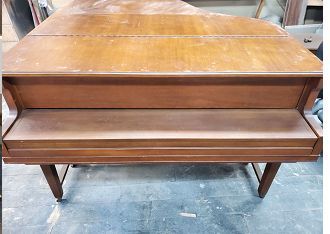 A wooden piano is sitting on a concrete floor in a room.