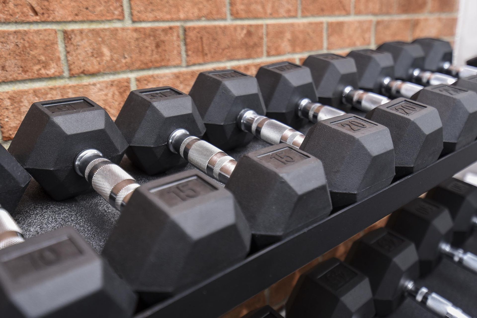 Row of black dumbbells on a rack against a brick gym wall at Holly Court, offers apartments near Rowan University.