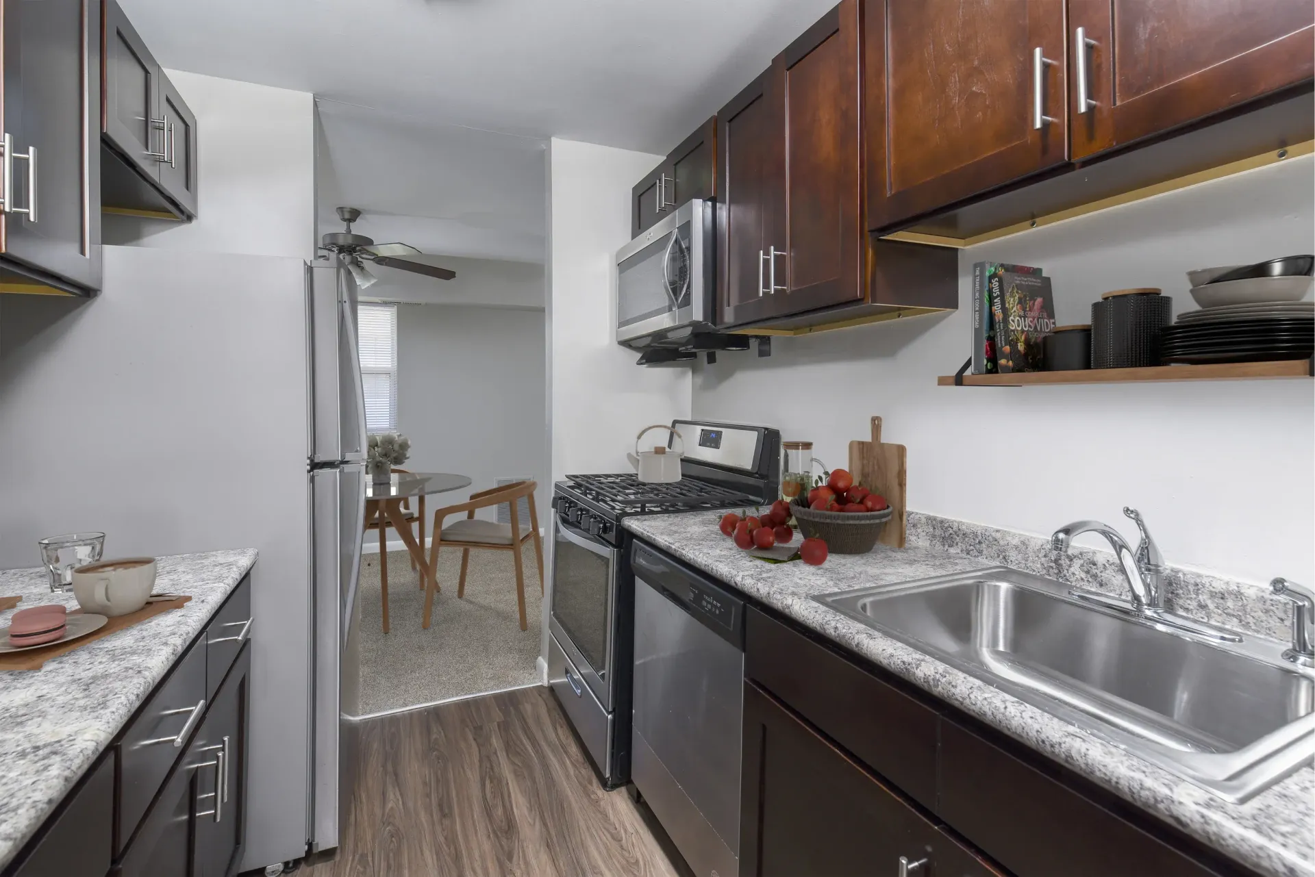 Galley-style apartment kitchen with dark wood cabinets, stainless appliances, and granite countertops at Holly Court, offers apartments for rent in Pitman, NJ.