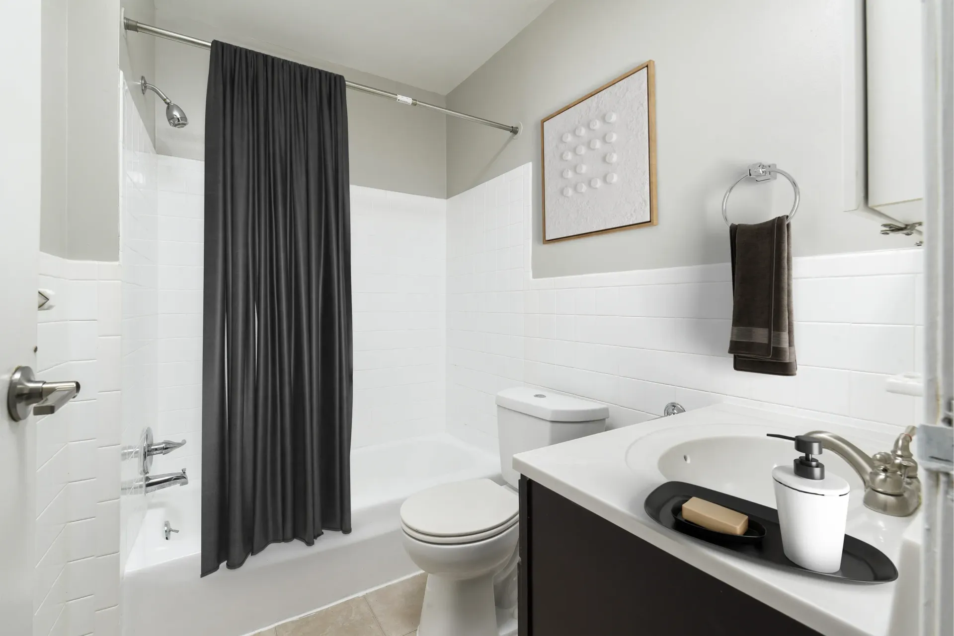 Bathroom with tub/shower, white tile surround, dark shower curtain, toilet, and sink at Holly Court, offers apartments in Pitman, NJ.