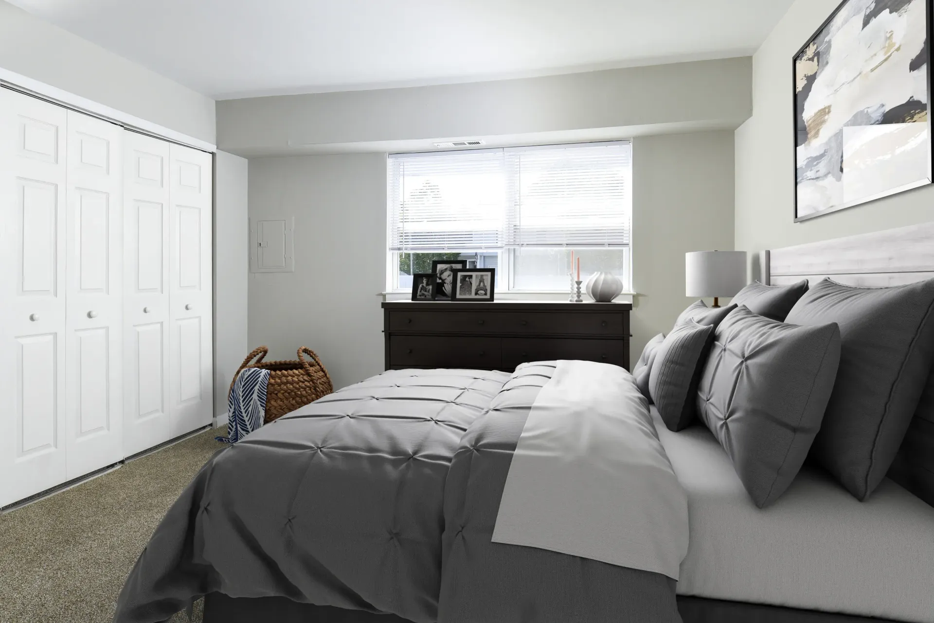 Bedroom with gray bedding, dark dresser, and window with blinds at Holly Court, offers apartments for rent in Pitman, NJ.