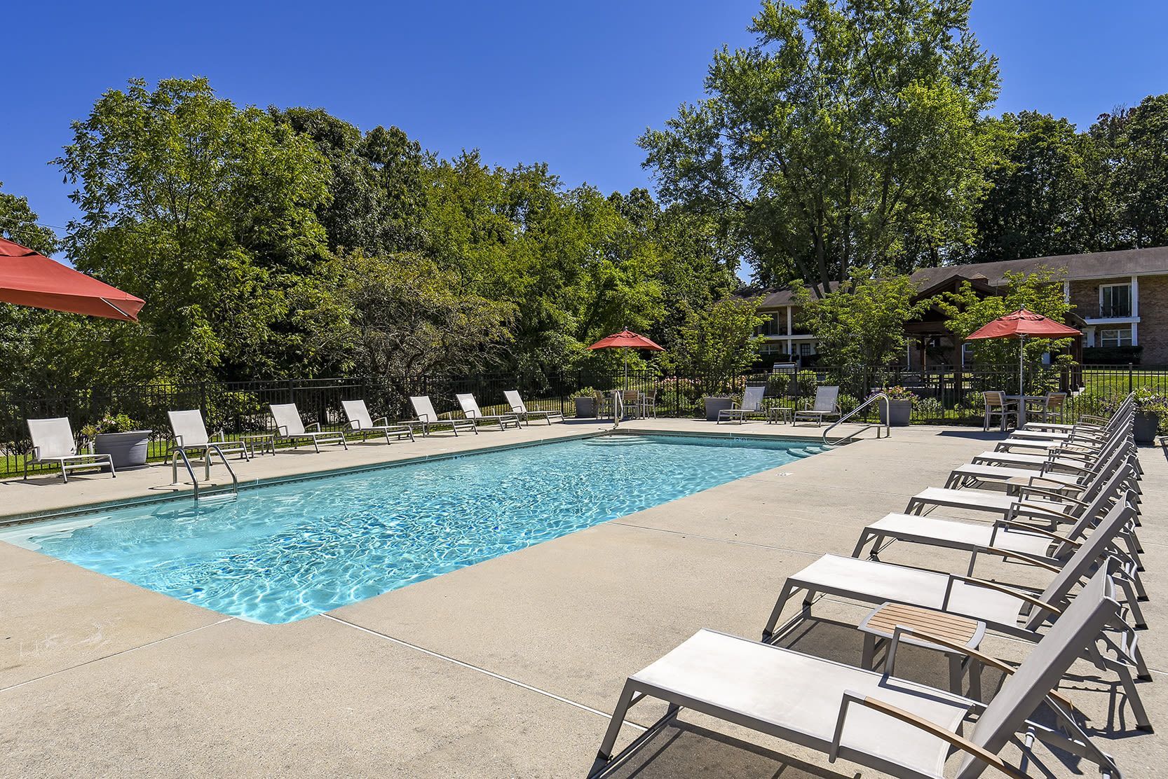 Outdoor pool with lounge chairs and red umbrellas, surrounded by trees at Holly Court, offers apartments near downtown Pitman, NJ.