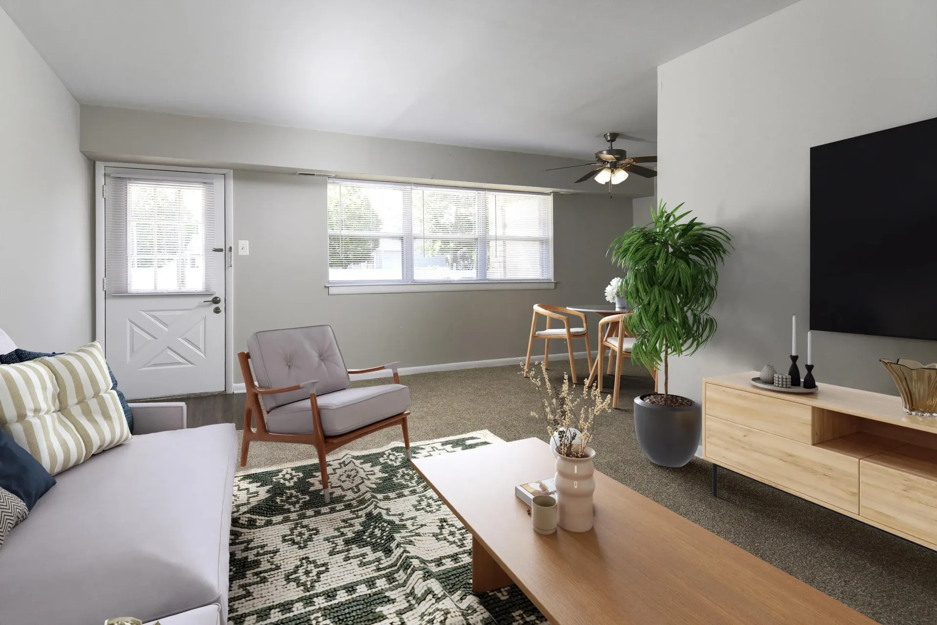 Living room in an apartment with sofa, armchair, coffee table, TV, plant, and dining area at Holly Court, offers apartments for rent in Pitman, NJ.