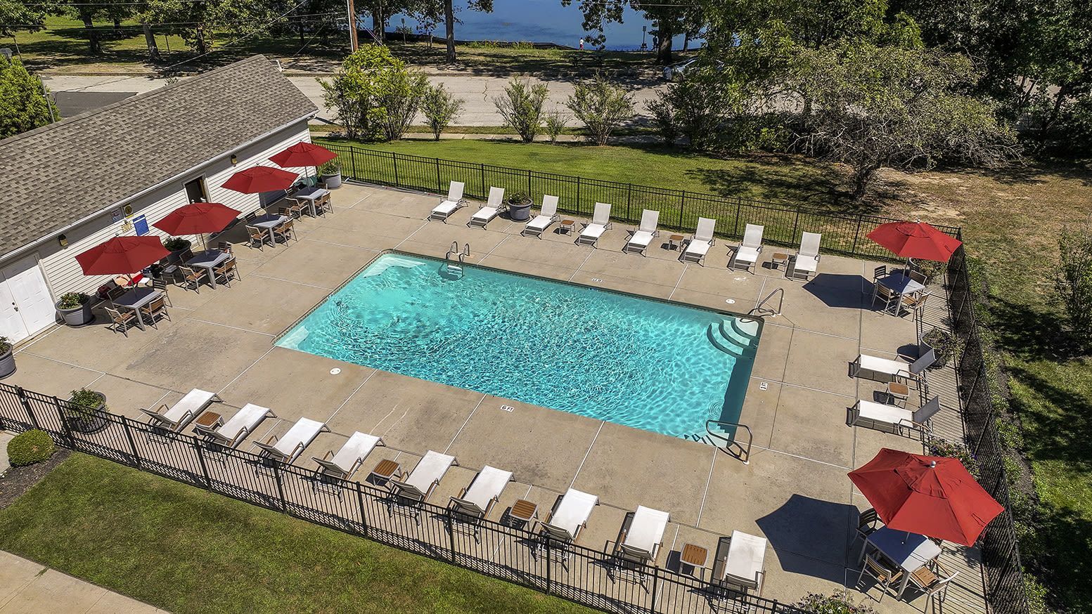 Aerial view of a community pool area with lounge chairs and red umbrellas at Holly Court, offers apartments in Pitman, NJ.