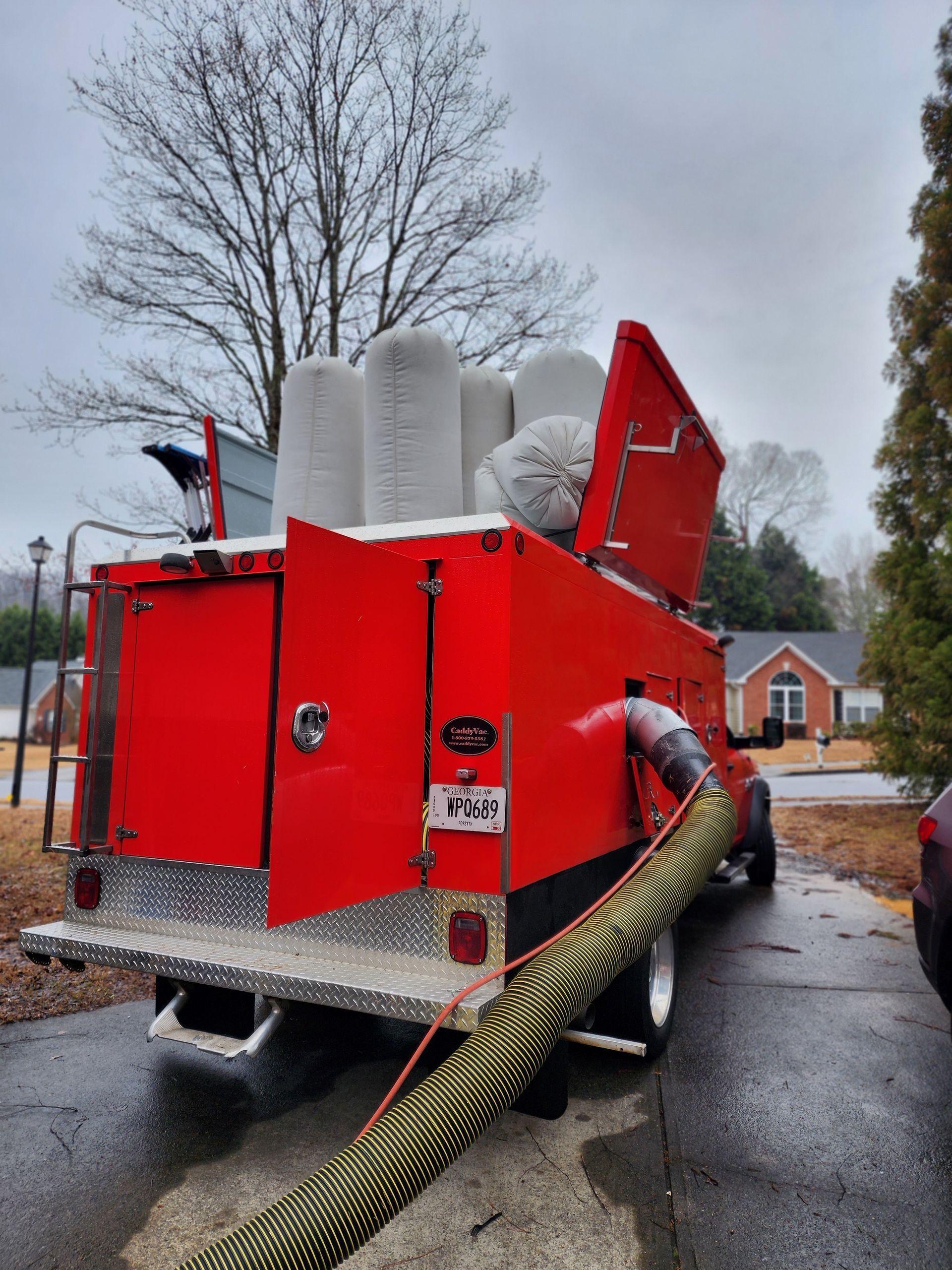 A red truck with a hose attached to it is parked in a driveway.