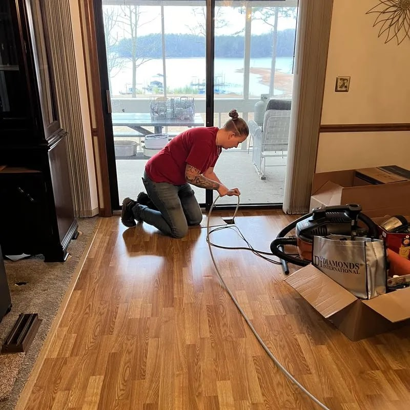 Person kneeling on floor near sliding door, working with a cable; lake view.