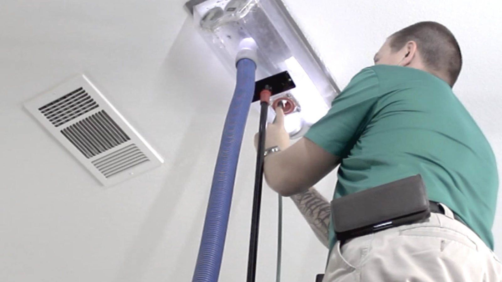 A man is cleaning a vent with a vacuum cleaner.