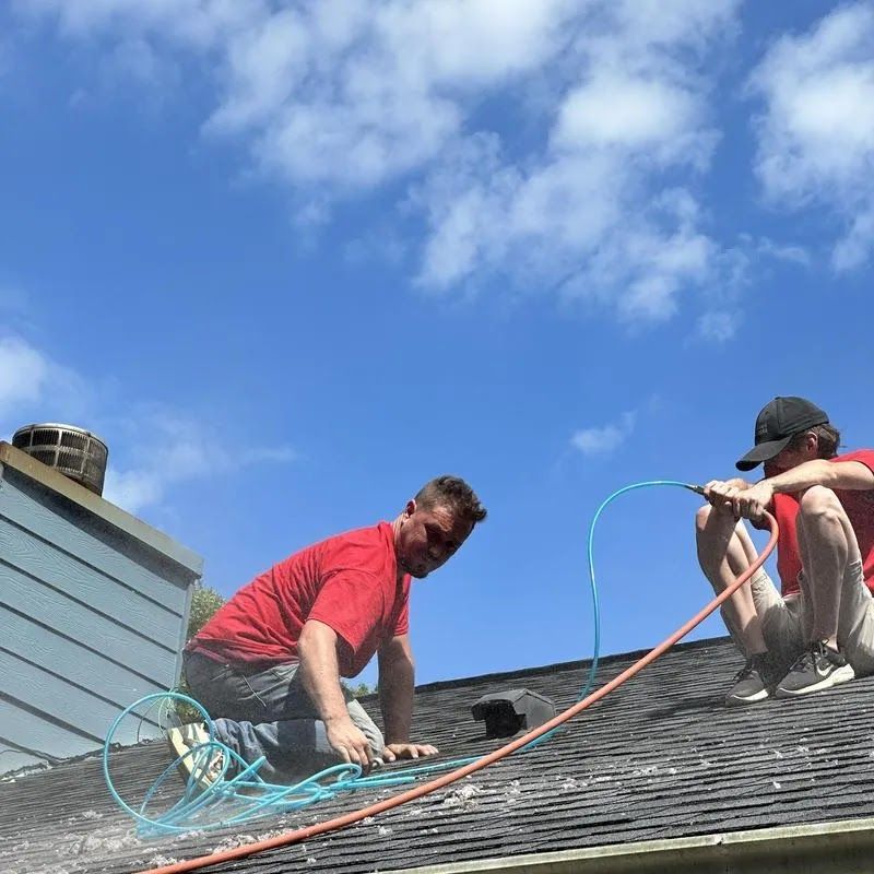 Two workers on a roof handling coiled cables under a blue sky