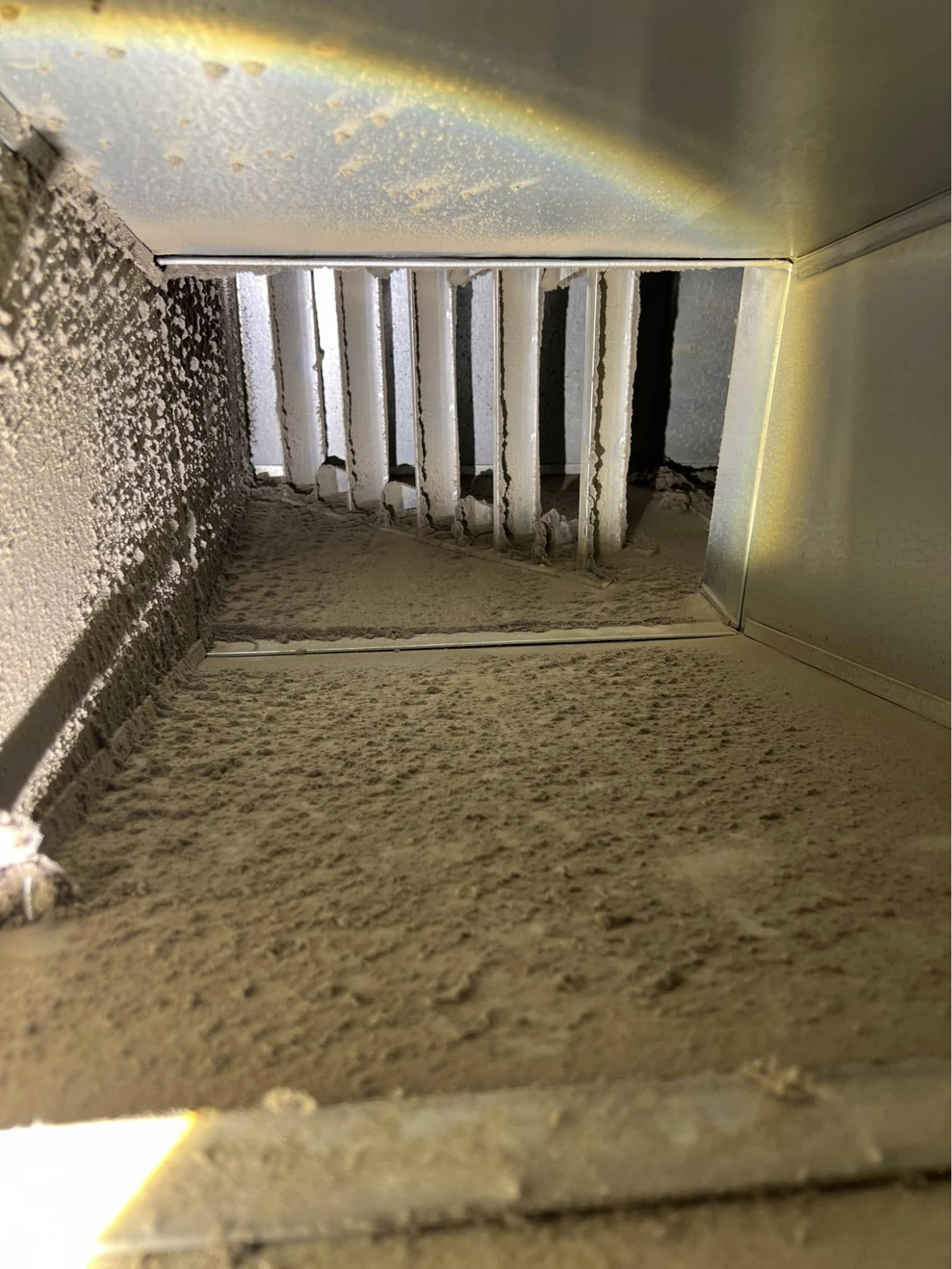 Interior view of a residential air vent duct covered in a thick layer of grey dust and debris.