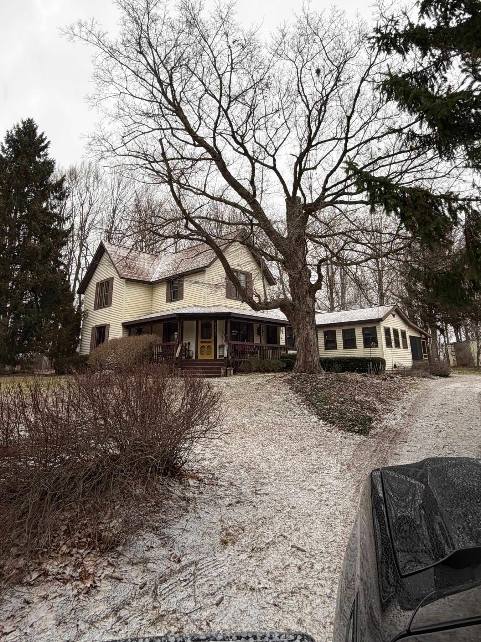 Snowy suburban house with large leafless tree and parked car in the foreground