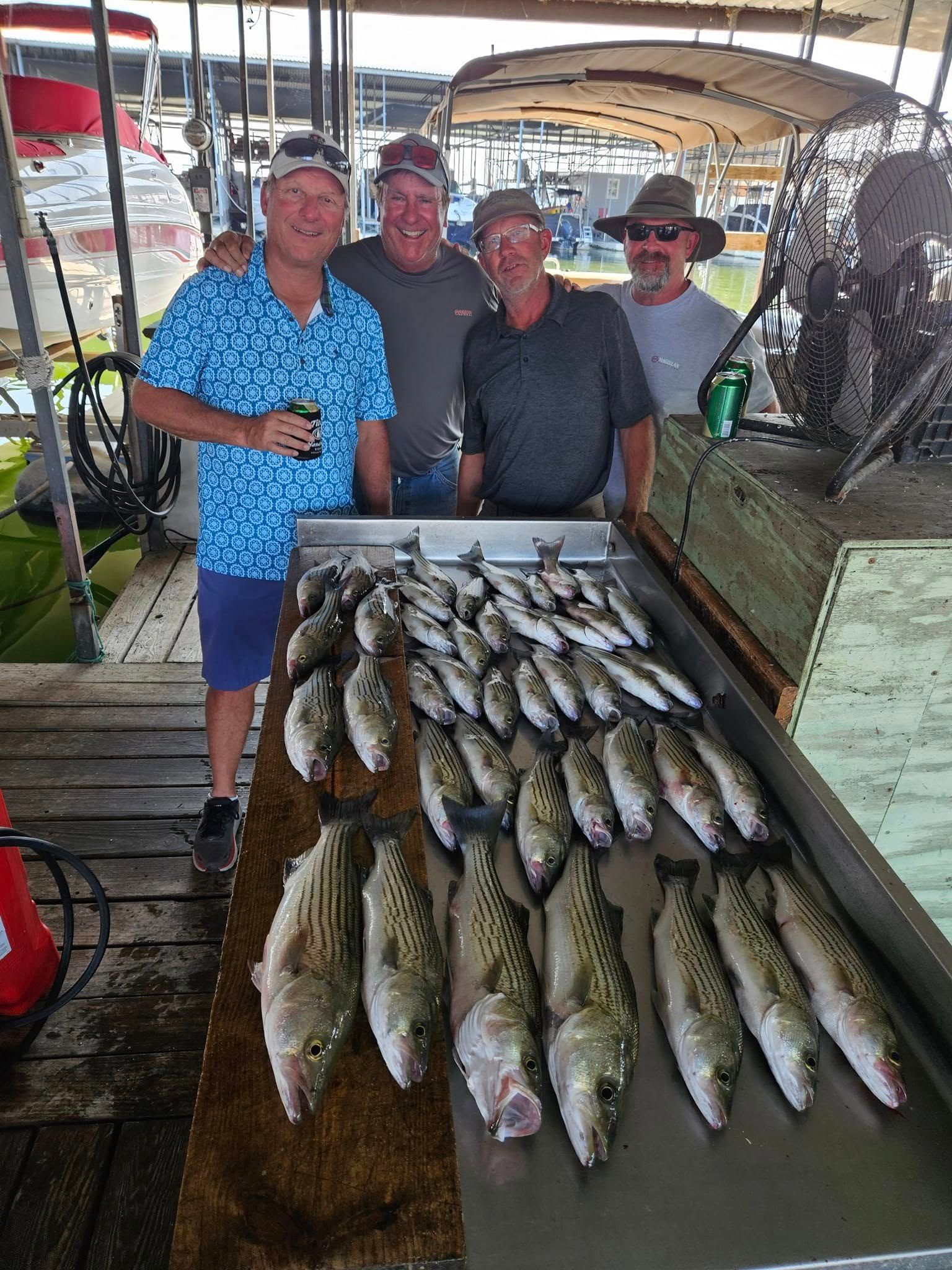 Four men pose with their catch of fish on a cleaning table at a dock.