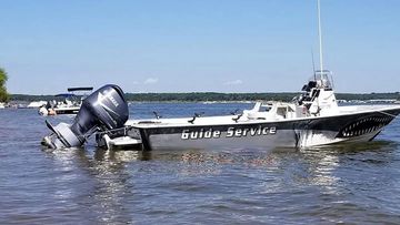 A fishing boat with a shark mouth design on the side is in the water. The words 