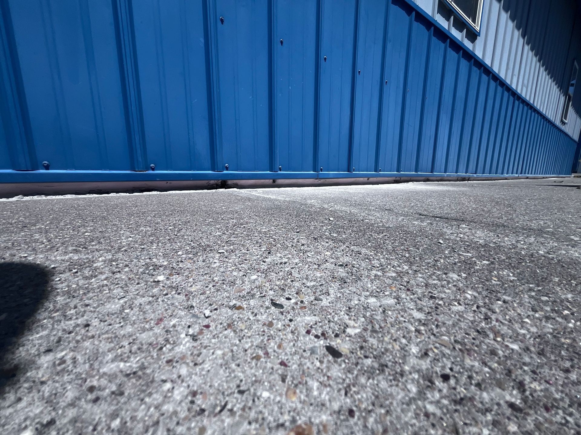 Blue metal fence beside a rough concrete pavement in bright daylight