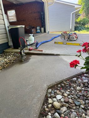 Patio being pressure washed with hose, equipment, and gravel border beside a garage.