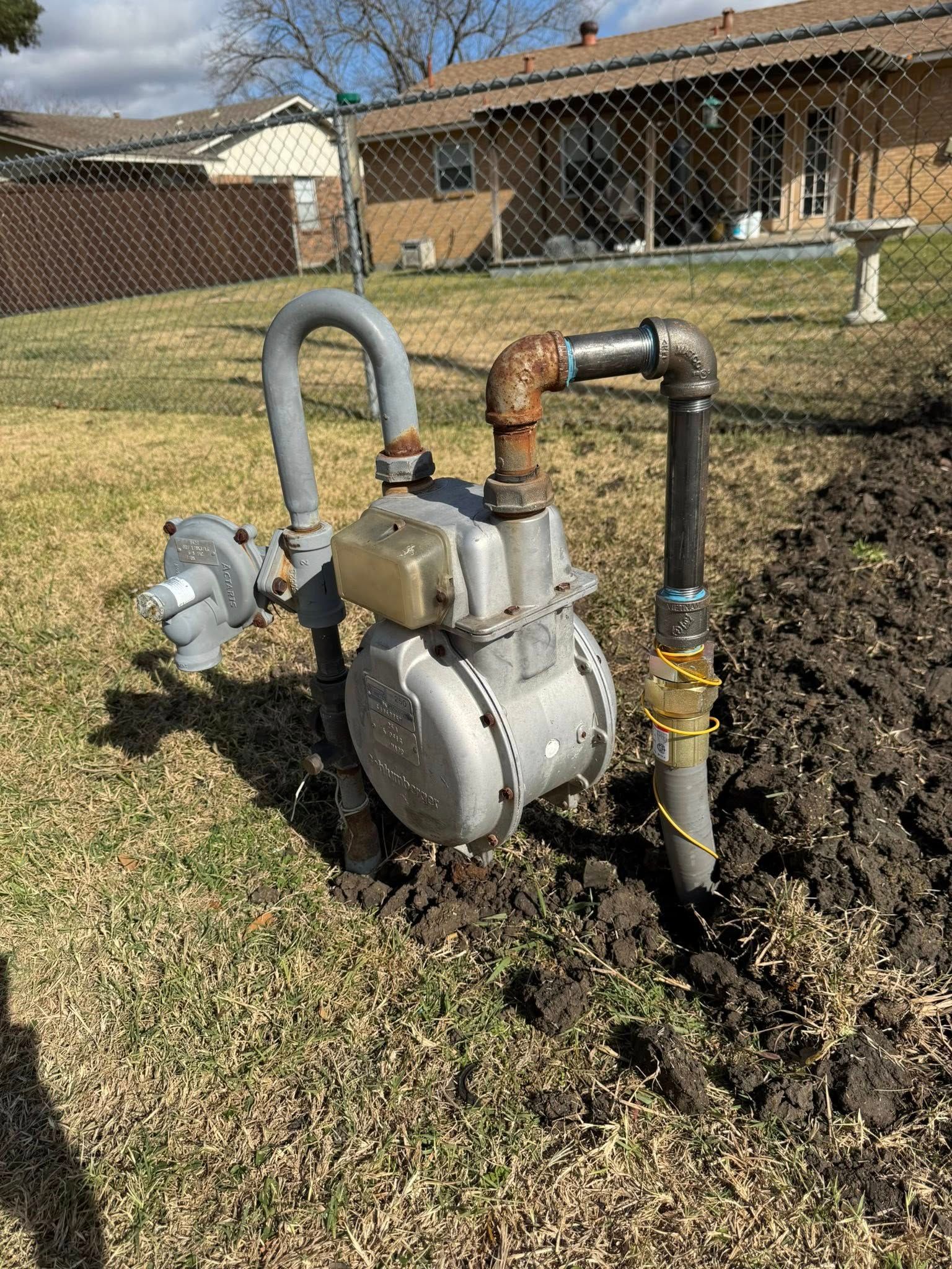 A natural gas meter assembly with a grey regulator and piping installed in a residential backyard lawn.